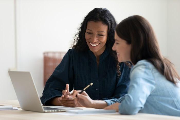 Close up happy young businesswoman using laptop with laughing female mentor