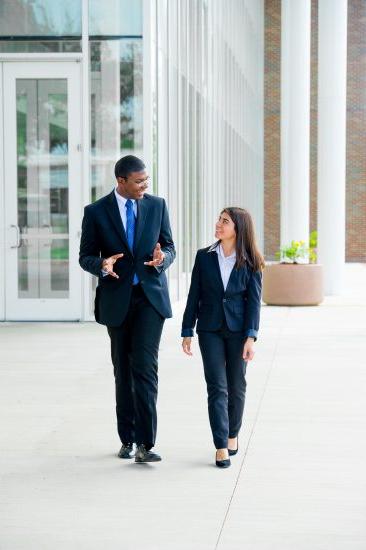 A female and male business dress walking outside talking.