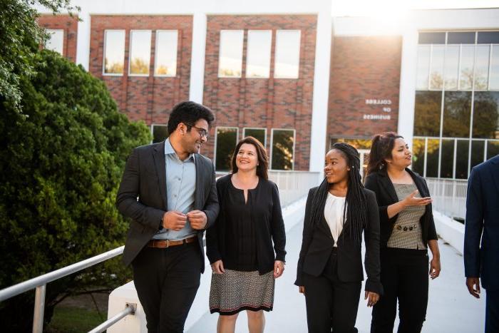 A big of students walking out of the business building smiling and talking.